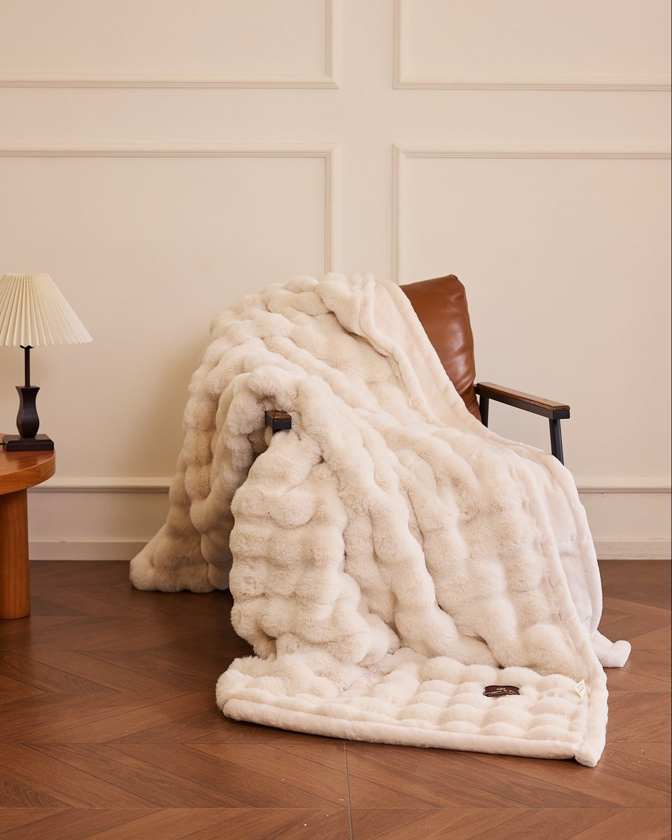 White fur throw blanket draped over a chair in a room with wooden flooring and a lamp.